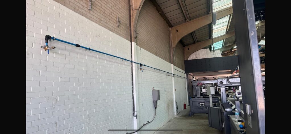 Blue aluminium compressed air ring main running along a modern factory wall with machine drops